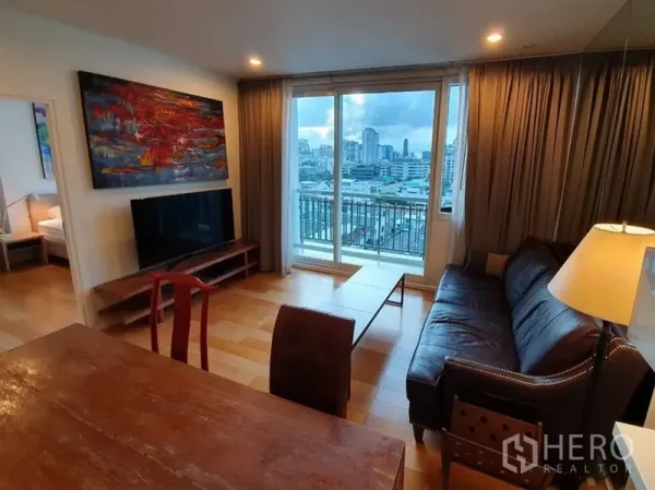คอนโด ให้เช่าในWatthana, Bangkok - ห้องนั่งเล่นพร้อมโซฟาหนัง ชั้นวางทีวี และประตูกระจกสไลด์ออกไประเบียงวิวเมือง