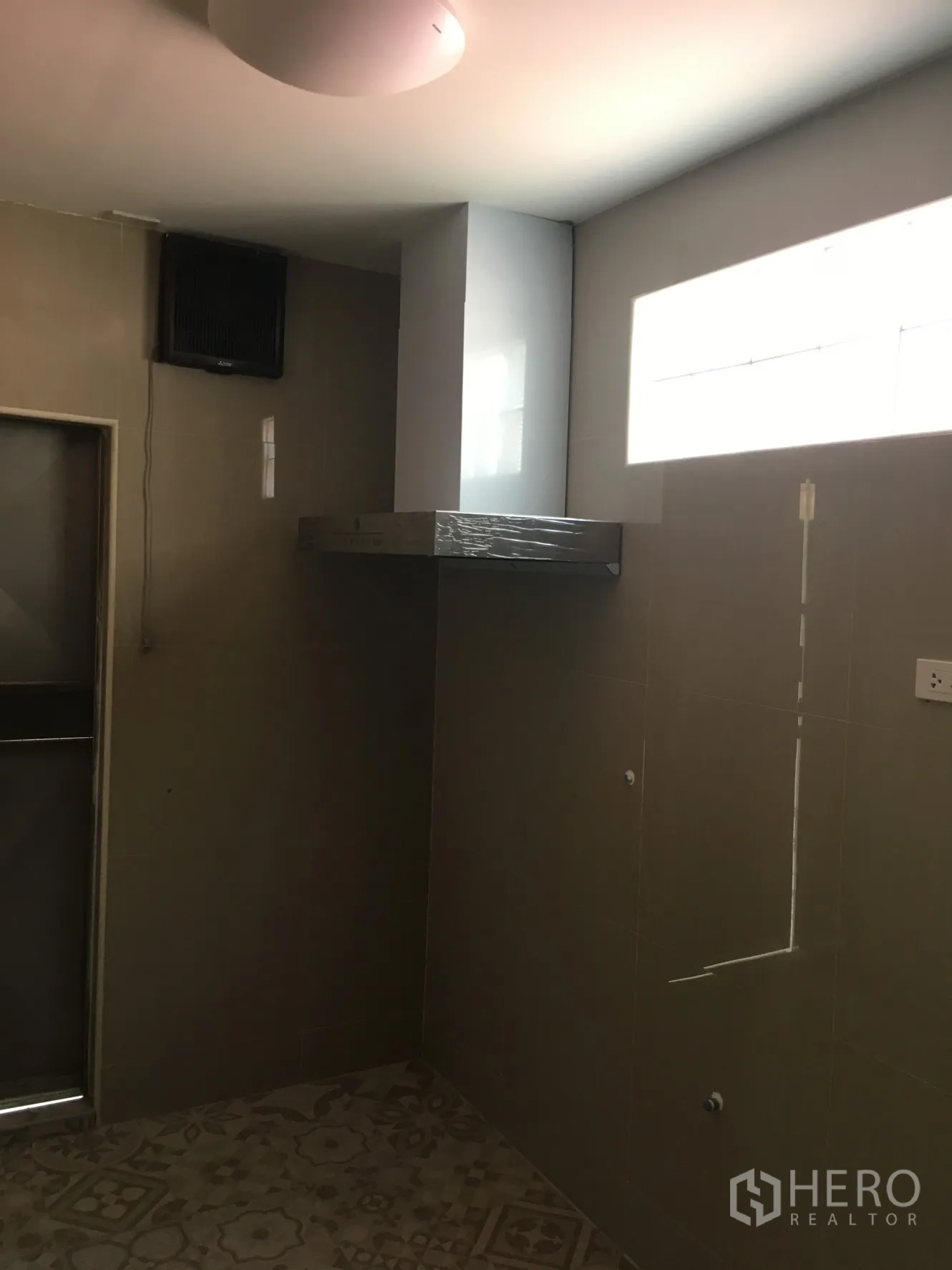 Townhouse for rent in Huai Khwang, Bangkok - Simple Thai kitchen with tiled walls, ventilation hood and patterned floor tiles.