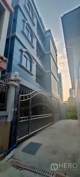 带办公室的家 出租在Pathum Wan, Bangkok - 傍晚视角的蓝灰色家庭办公楼立面与大门入口。