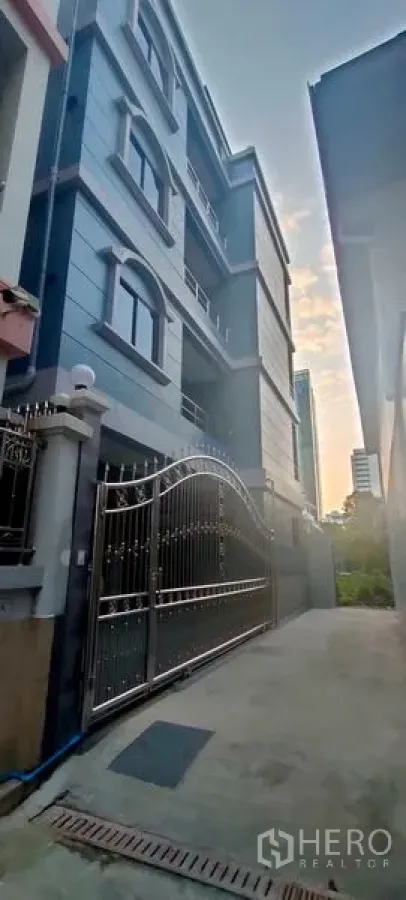 带办公室的家 出租在Pathum Wan, Bangkok - 傍晚视角的蓝灰色家庭办公楼立面与大门入口。