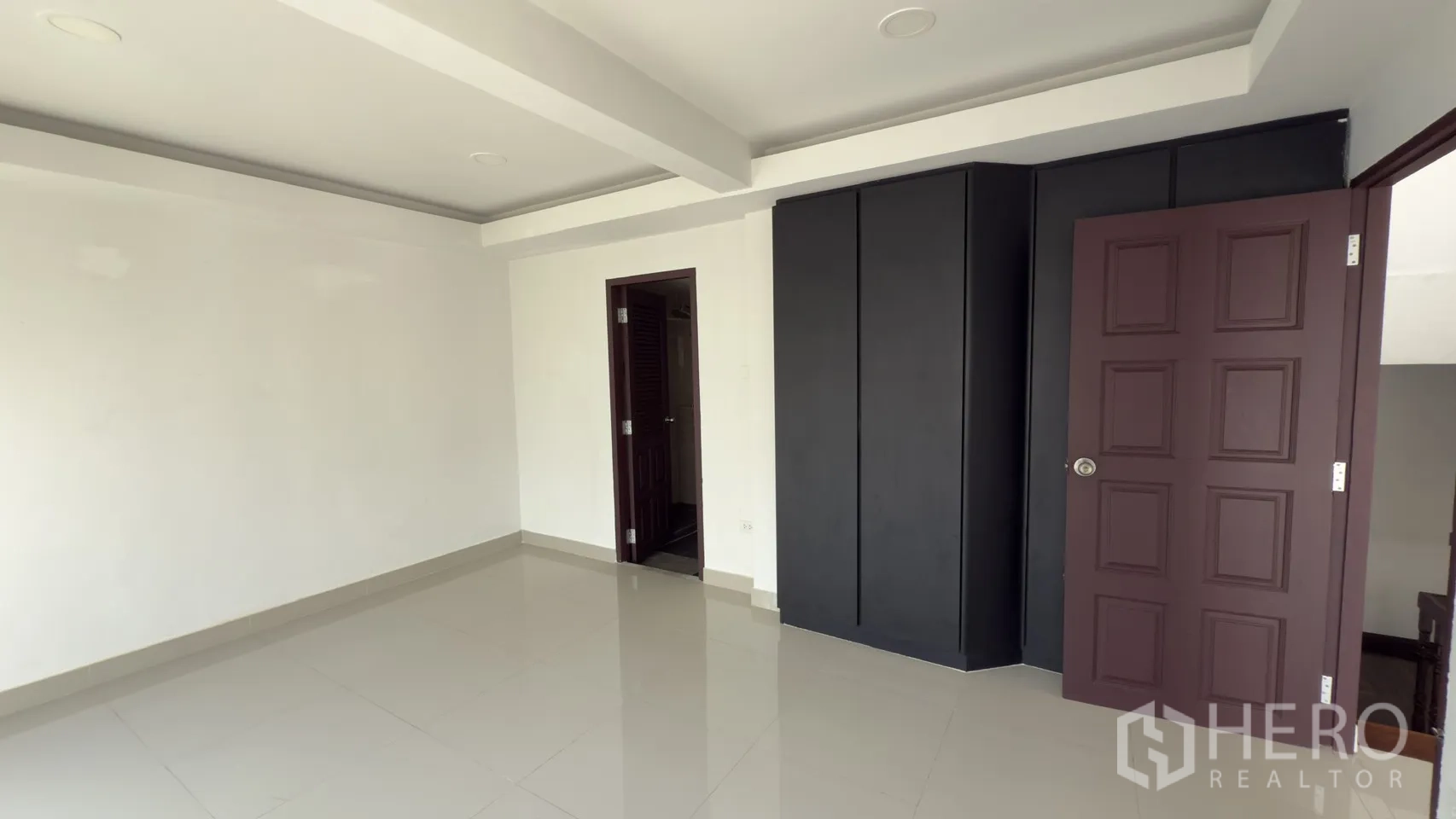 联排别墅 for rent in Watthana, Bangkok - 卧室内置黑色衣柜，旁有通往瓷砖浴室的门。
