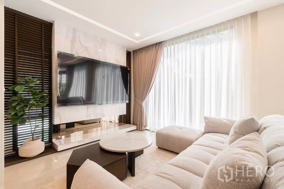 Detached House for rent or sale in Prawet, Bangkok - Close view of TV wall, marble console and soft sectional sofa by tall windows