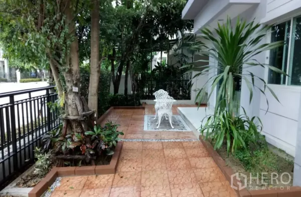 Detached House for rent in Saphan Sung, Bangkok - Front patio garden with mature trees, white outdoor chairs and tiled path