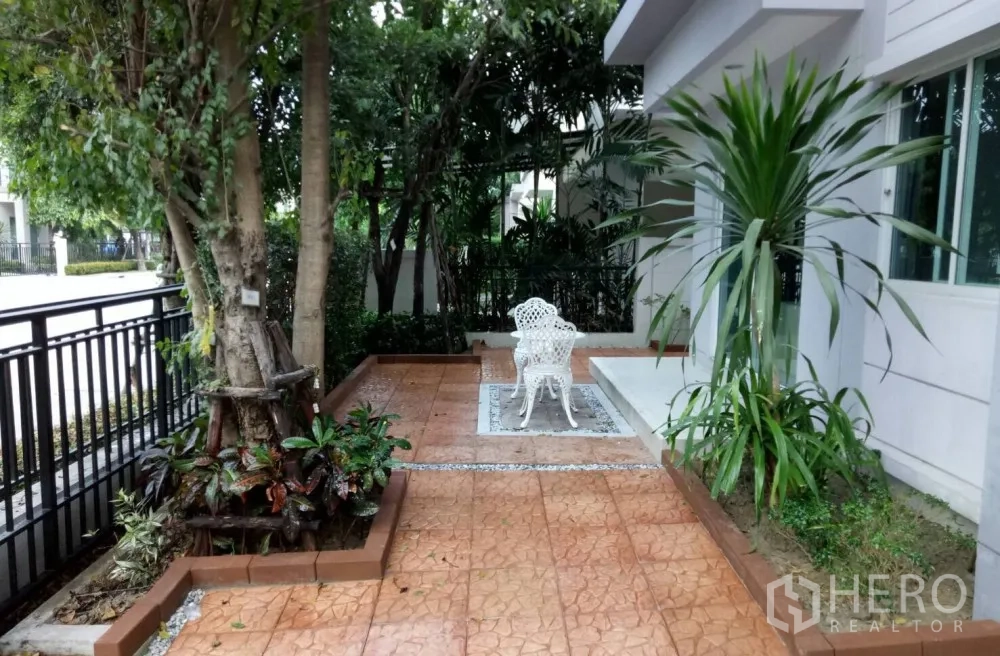 Detached House for rent in Saphan Sung, Bangkok - Front patio garden with mature trees, white outdoor chairs and tiled path