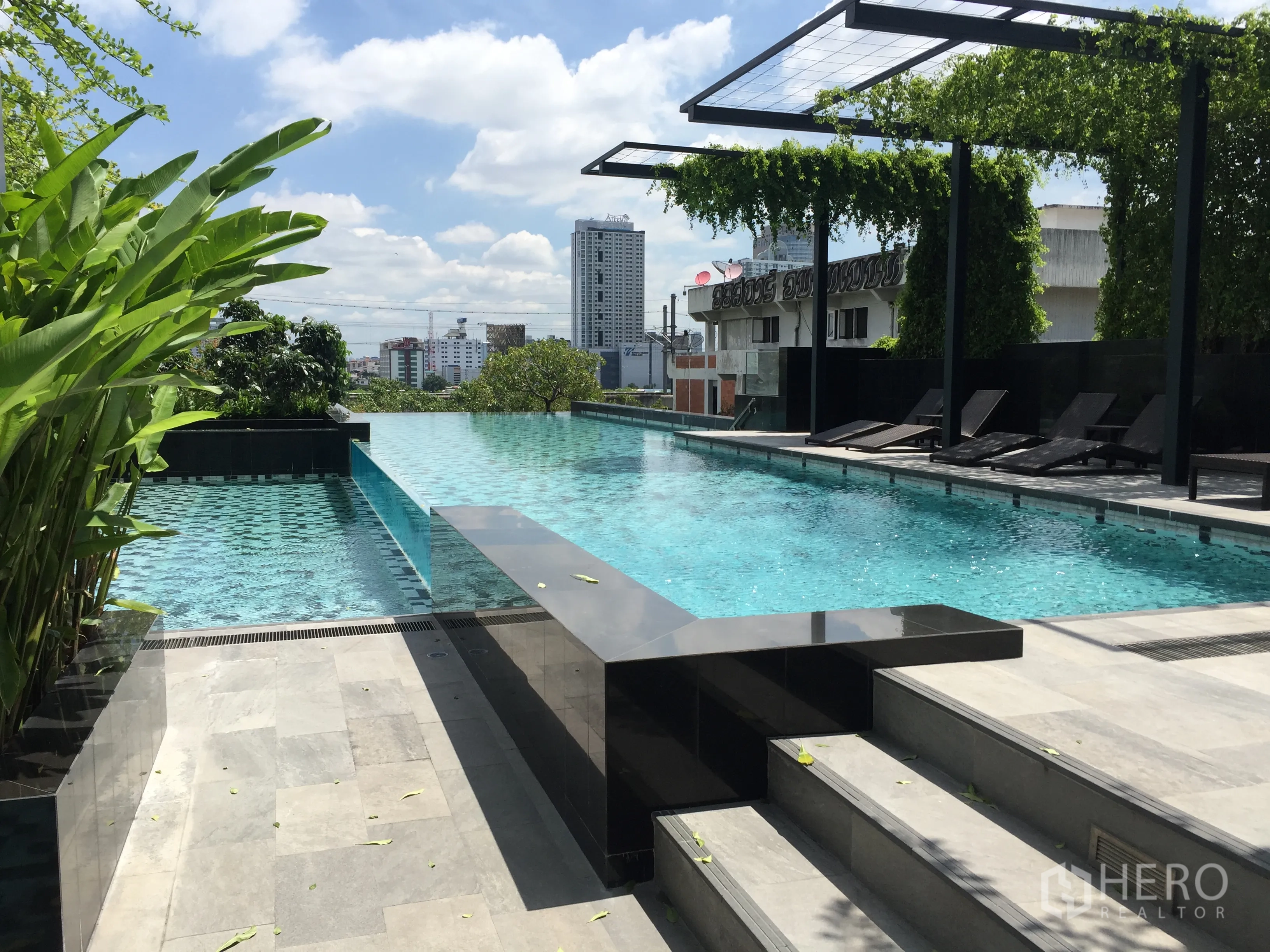 Condominium for rent in Ratchathewi, Bangkok - Rooftop infinity-edge swimming pool with sun loungers and city backdrop.