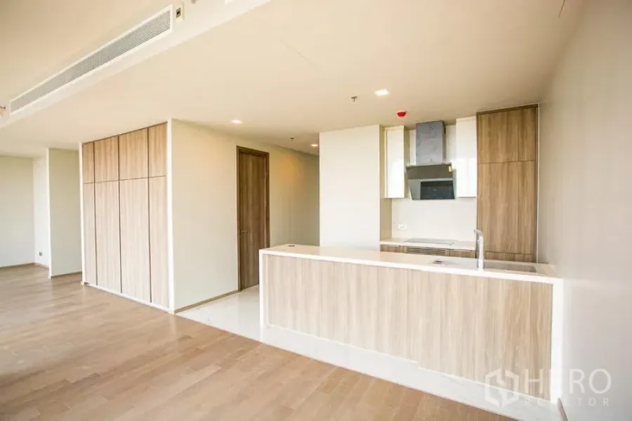 Condominium for rent in Watthana, Bangkok - Open-plan condo kitchen with wood cabinetry, white island counter, and recessed lighting.