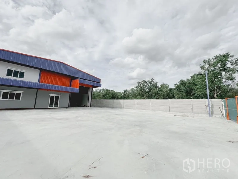 货栈 出租或出售在Khlong Luang, Pathum Thani - 仓库侧的大型混凝土堆场，高卷闸装卸口、围墙与绿化背景。