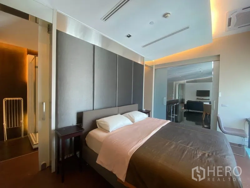 Condominium for rent in Sathon, Bangkok - Primary bedroom with padded headboard, warm cove lighting and sliding door to the ensuite bathroom.