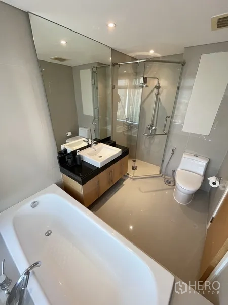 Condominium for rent or sale in Watthana, Bangkok - Modern bathroom with bathtub, glass shower enclosure, large mirror, vanity, and toilet.