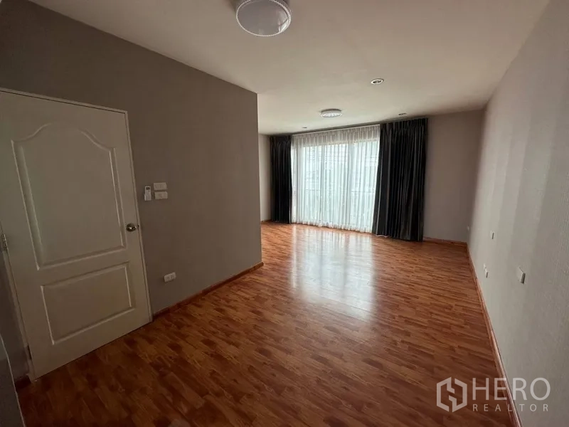 Townhouse for rent or sale in Phra Khanong, Bangkok - Large bedroom with wood flooring and sheer curtains to the balcony.