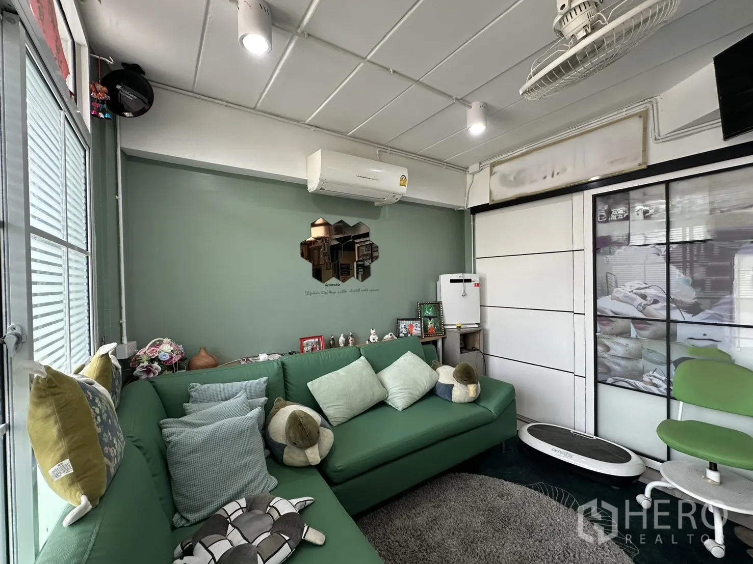 Shophouse for rent in Phra Khanong, Bangkok - Cozy lounge with green sectional sofa, air conditioner, and sliding door.