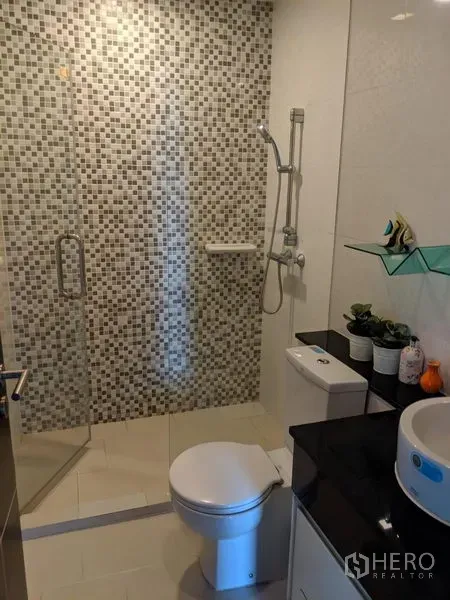 公寓 出租在Watthana, Bangkok - 浴室设玻璃淋浴间，马赛克墙砖、洗手台与坐便器。