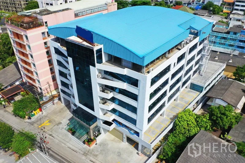 Office Space for rent in Khlong Toei, Bangkok - Aerial view of a modern mid-rise office building with a blue roof and on-site parking in Khlong Toei, Bangkok.