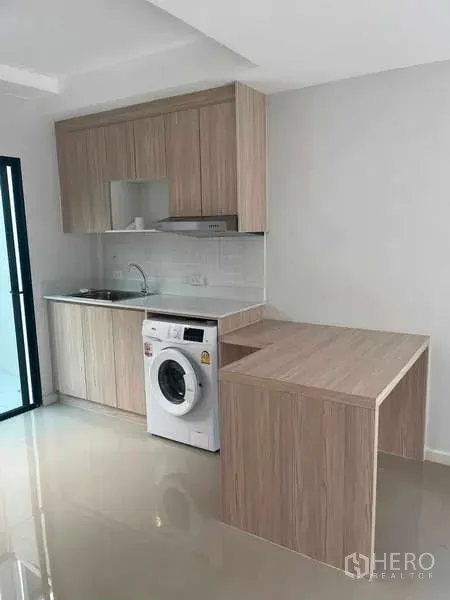 Townhouse for rent in Suan Luang, Bangkok - Modern light-wood kitchenette with cabinets, sink, cooktop, peninsula counter and washing machine.