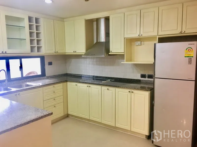 公寓 出租在Watthana, Bangkok - 宽敞U型厨房，奶油色橱柜、花岗岩台面、灶台与抽油烟机，并带窗户。