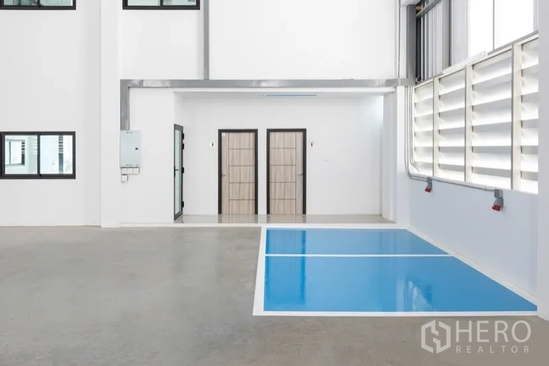 Warehouse for rent in Bang Bo, Samut Prakan - Interior corner with blue marked work zone, louvered ventilation and two restroom doors.
