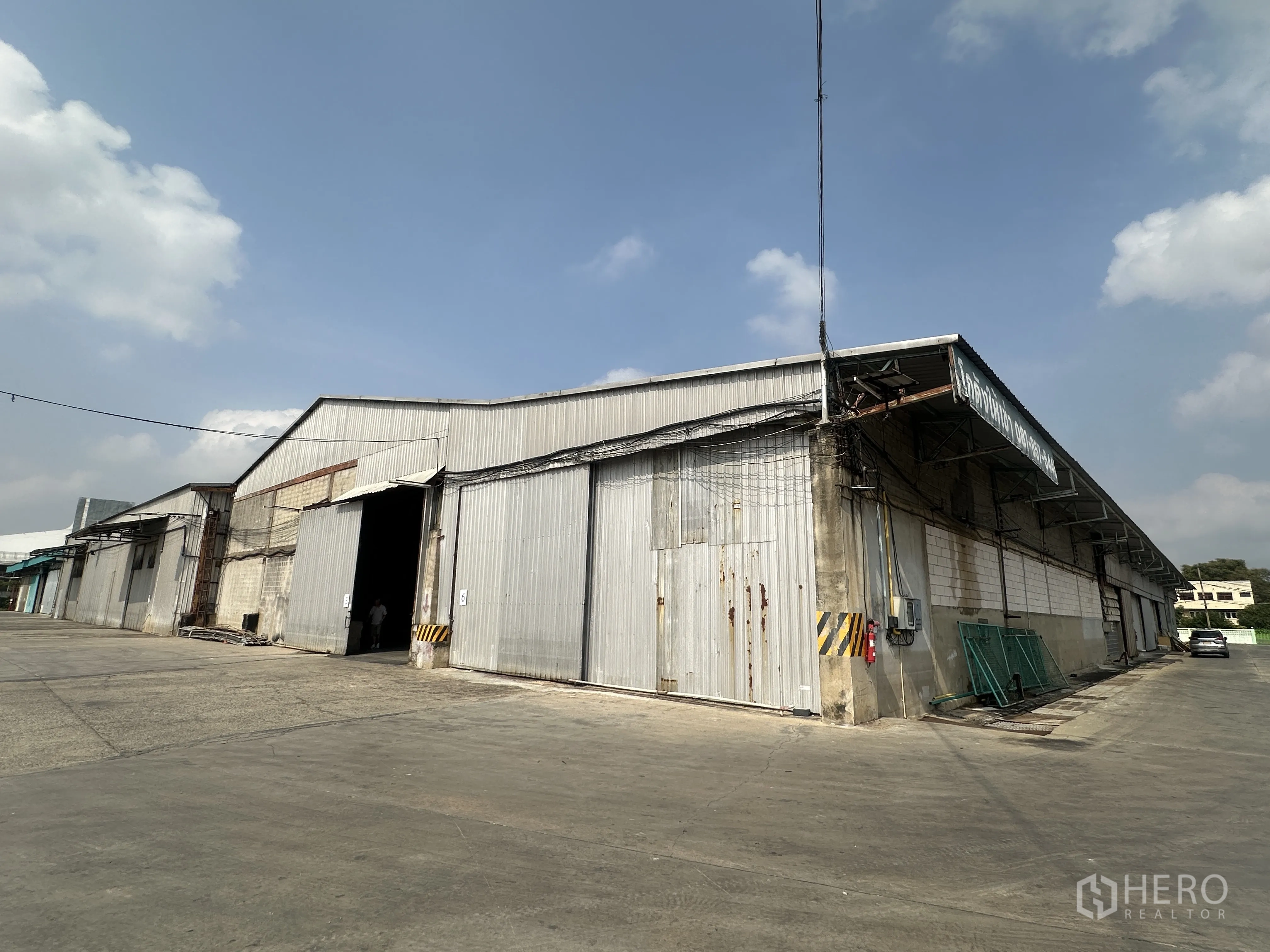 Warehouse for rent in Mueang Pathum Thani, Pathum Thani - Corner view of industrial warehouse with large sliding doors and a wide truck-access yard.