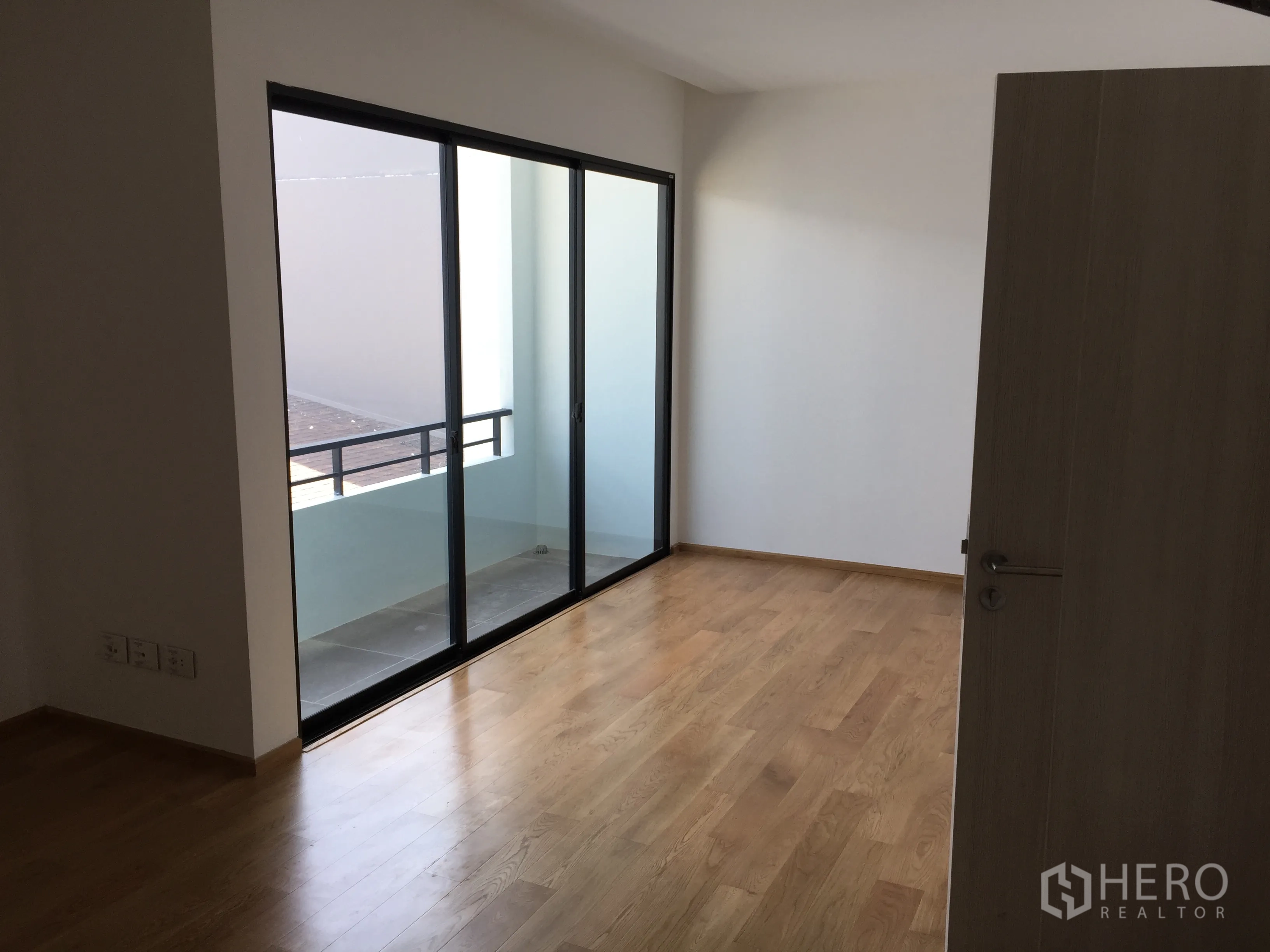 Townhouse for rent in Saphan Sung, Bangkok - Bedroom with wood floors and sliding door leading to a small balcony.