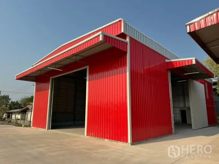 Warehouse for rent in Lam Luk Ka, Pathum Thani - Corner exterior of a bright red warehouse with loading canopy and wide driveway.
