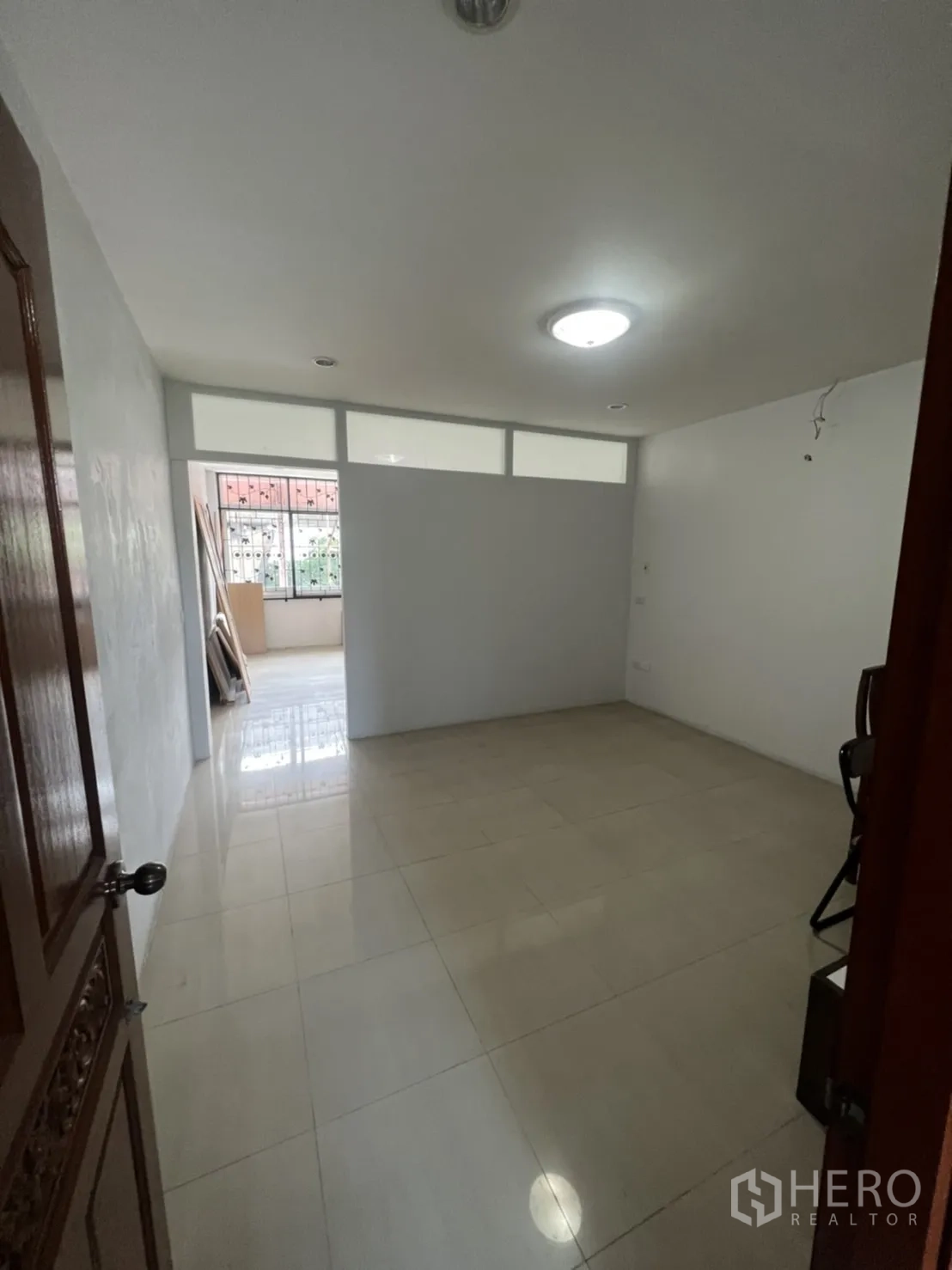 Shophouse for rent in Khlong Toei, Bangkok - Empty tiled room with a partition wall and ceiling lights for flexible layout.