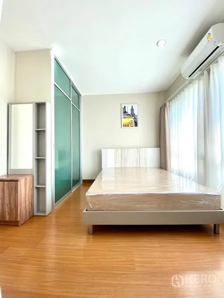Townhouse for rent in Prawet, Bangkok - Sunlit bedroom with air conditioning, green glass sliding wardrobe, and floor-to-ceiling windows.