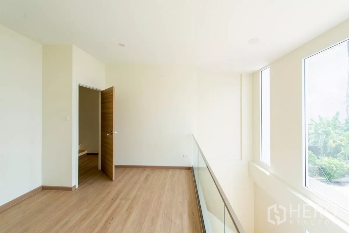 Townhouse for sale in Lat Phrao, Bangkok - Mezzanine hallway with glass balustrade overlooking the double-volume living area.