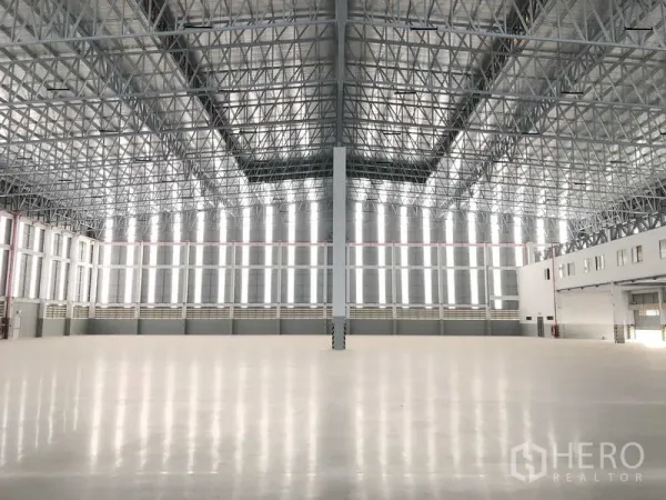 Factory for rent or sale in Samut Prakan - Expansive warehouse interior with super-flat polished floor and high steel truss roof admitting daylight.