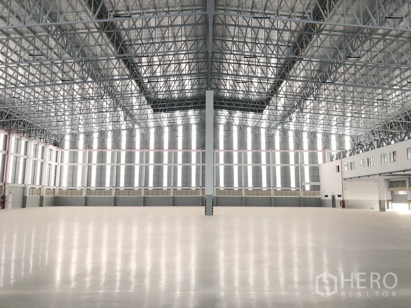 Factory for rent or sale in Samut Prakan - Expansive warehouse interior with super-flat polished floor and high steel truss roof admitting daylight.
