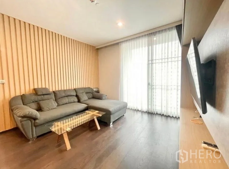 คอนโด ให้เช่าในWatthana, Bangkok - ห้องรับแขกอบอุ่น โซฟา L‑shape ผนังลายซี่ไม้ และผ้าม่านโปร่ง