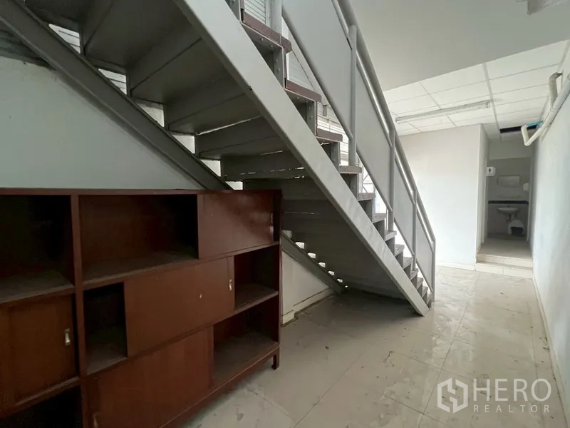 Shophouse for rent in Phra Khanong, Bangkok - Under-stair storage area with shelving and a glimpse of the restroom beyond.