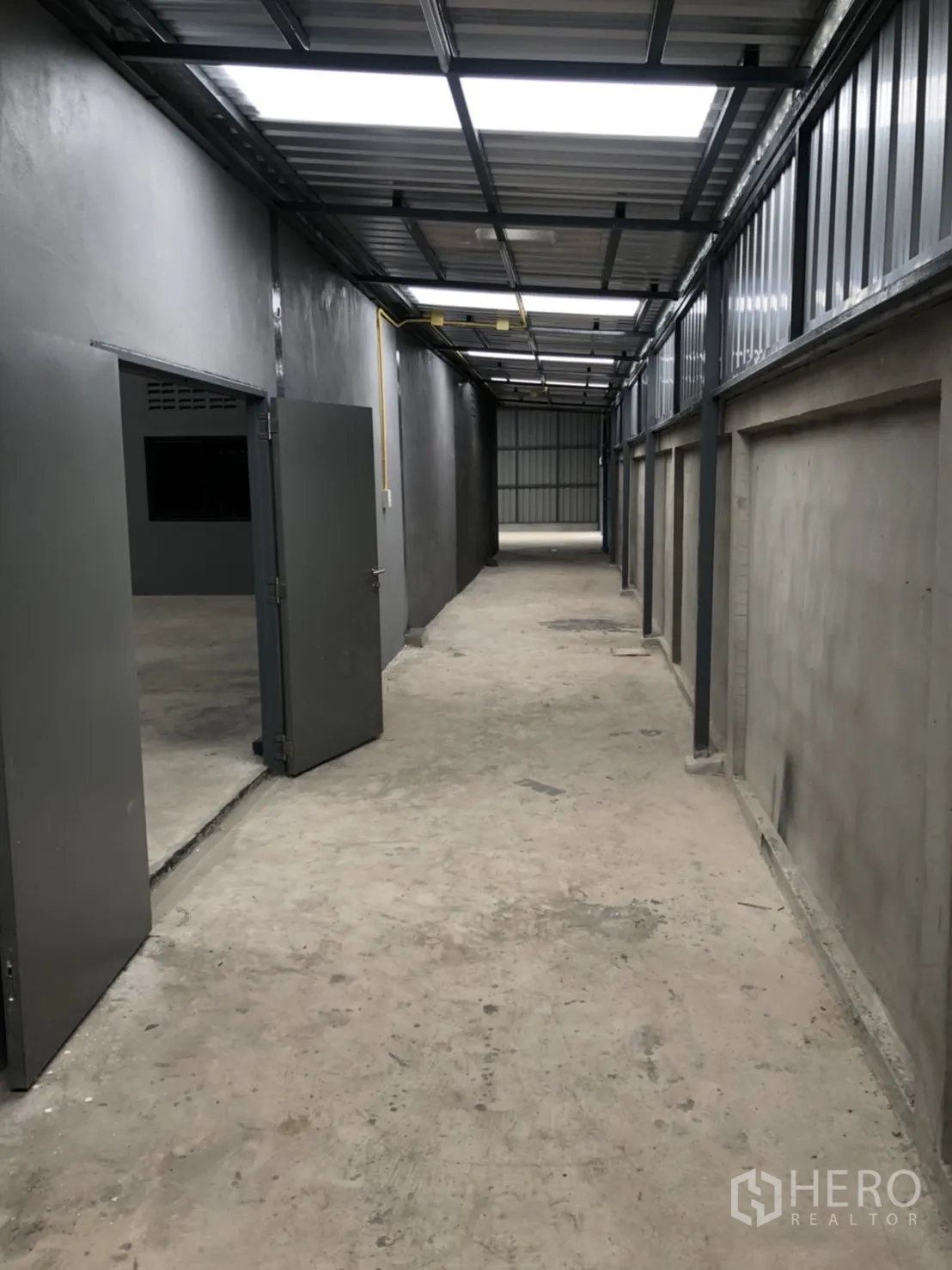 Warehouse for rent in Lam Luk Ka, Pathum Thani - Long roofed passageway with open doors to storage rooms and skylights above.