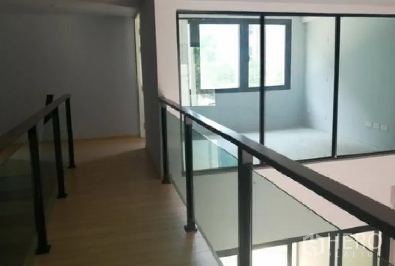 Townhouse for rent in Yan Nawa, Bangkok - Upper-floor corridor with glass balustrade overlooking a double-height space and a windowed room.