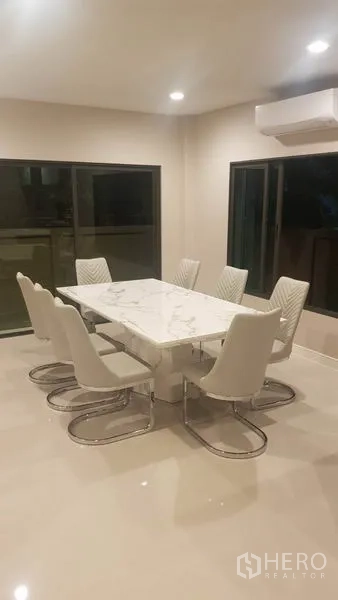 Detached House for rent in Saphan Sung, Bangkok - Dining area with a marble table and eight cushioned chairs under recessed lighting and large windows.