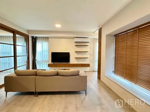 独立式住宅 出租或出售在Prawet, Bangkok - 采光充足的客厅，L型沙发、电视墙、搁架与空调。