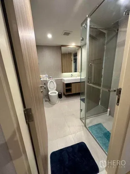 公寓 出租在Pathum Wan, Bangkok - 现代卫浴，玻璃淋浴房、洗手台、坐便器与中性色瓷砖。