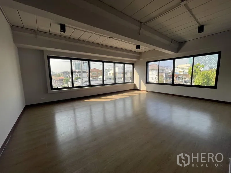 Home Office for rent in Phaya Thai, Bangkok - Sunlit room with panoramic city views through full-length windows and wood floors.