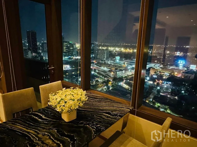 公寓 出租在Bangkok - 近景：岩纹餐桌与花艺，窗外是璀璨夜景