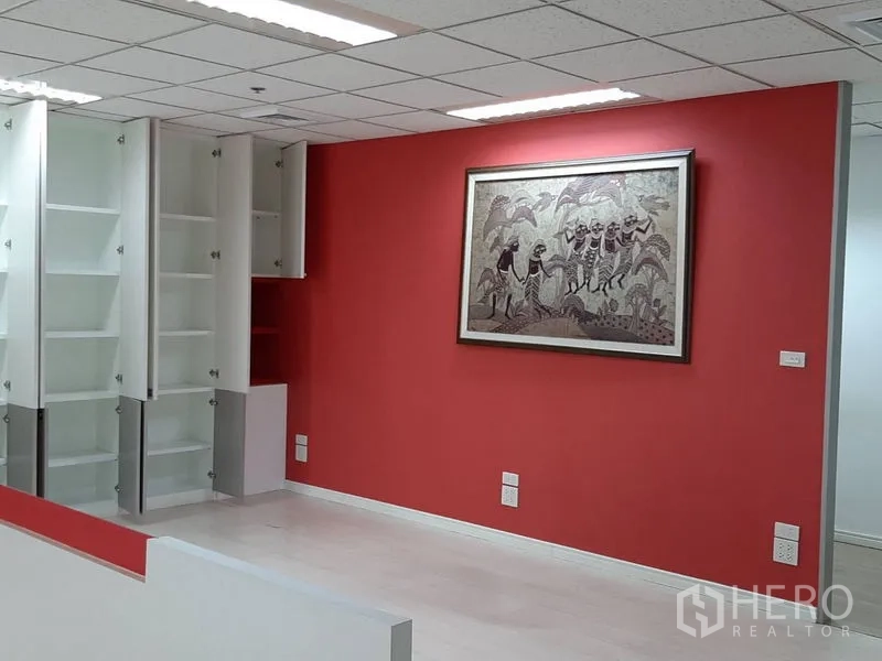 Office Space for rent in Bang Rak, Bangkok - Fitted office area with red feature wall, framed art and open white storage cabinets.