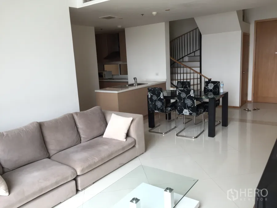 Condominium for rent in Sathon, Bangkok - Bright open-plan living room with sofa, glass coffee table, dining set, compact kitchen and an internal staircase.
