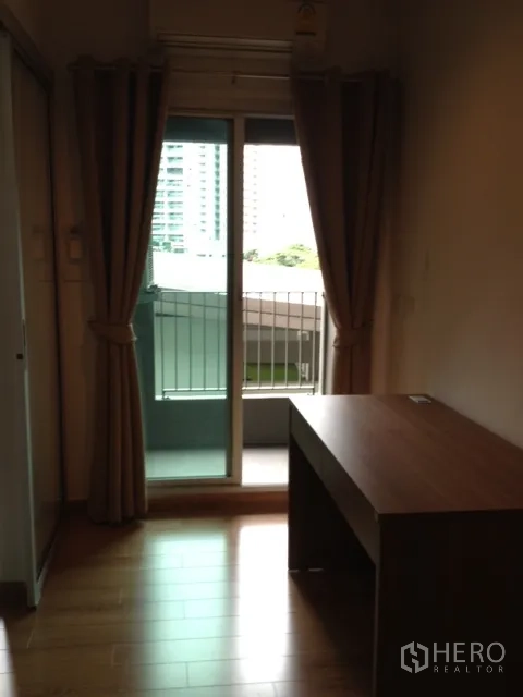 公寓 出租在Khlong Toei, Bangkok - 玻璃门通往小阳台，可见城市景观，配棕色窗帘与书桌。