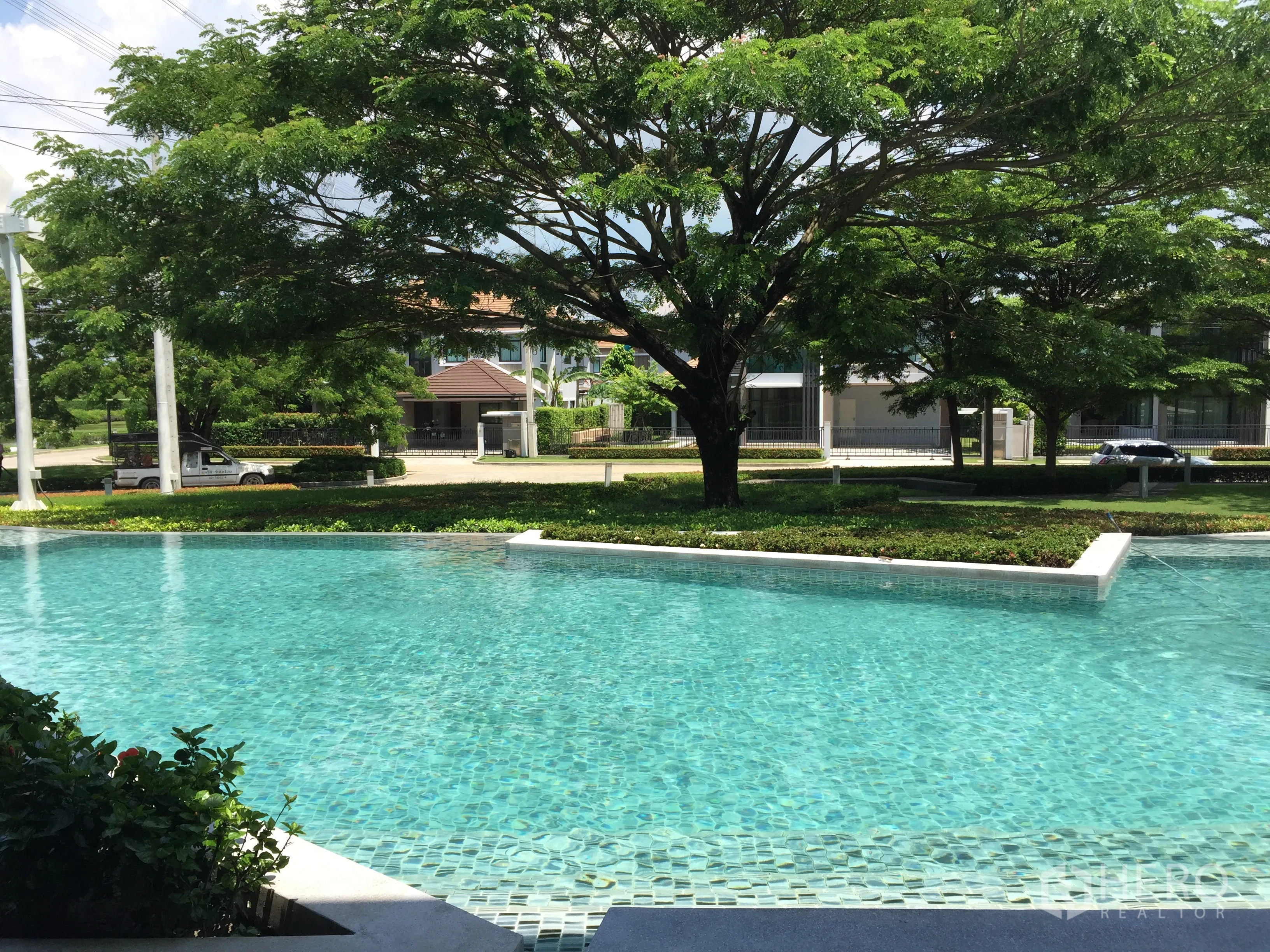 Detached House for rent or sale in Prawet, Bangkok - Outdoor swimming pool with clear blue water surrounded by trees and gardens.