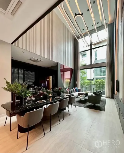 Detached House for rent or sale in Suan Luang, Bangkok - Dining area with long black table, eight chairs, tall windows, and modern light fixtures.