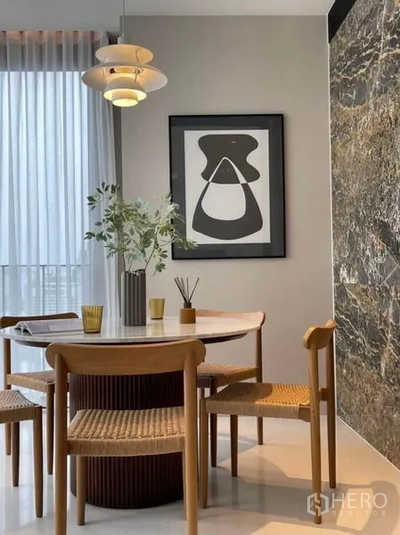 Condominium for rent or sale in Khlong Toei, Bangkok - Close-up of contemporary dining area with wooden chairs, framed artwork, and sheer curtains.