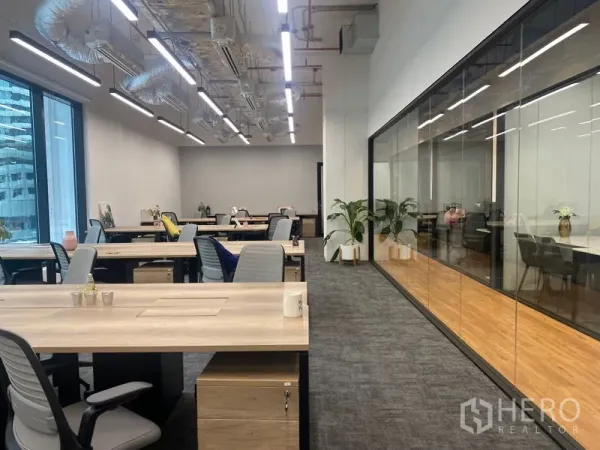 Office Space for rent in Pathum Wan, Bangkok - Modern open-plan office with long workstations, ergonomic chairs, carpet flooring, glass-walled meeting room, exposed ceiling ductwork, and large windows with city views.