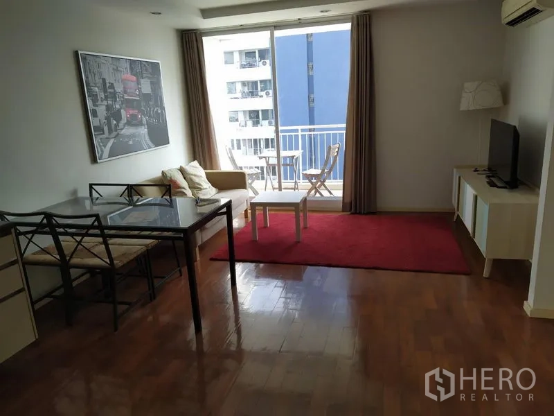 Condominium for sale in Khlong Toei, Bangkok - Living room facing the balcony with TV console and red area rug, city outlook.