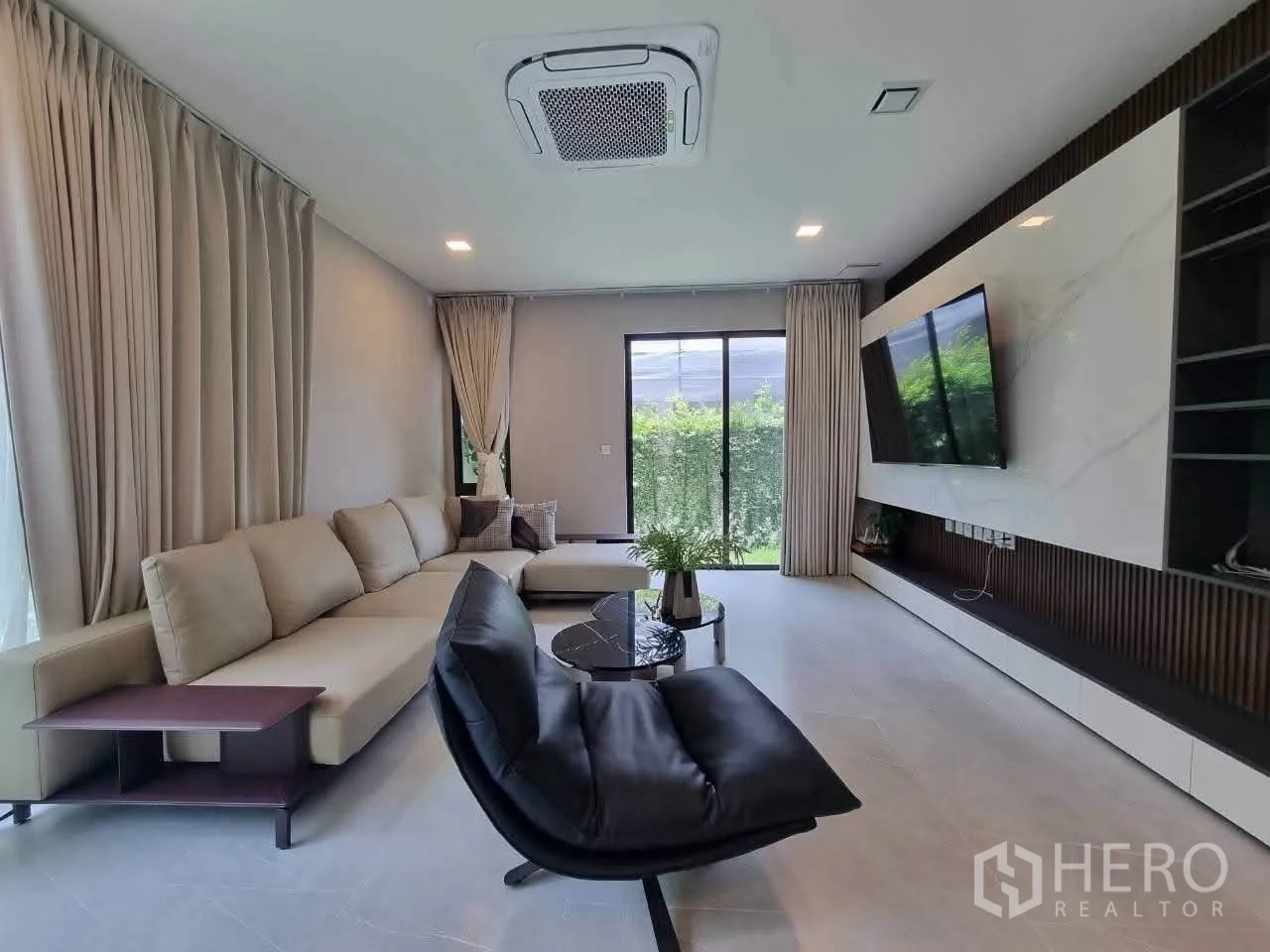 独栋房屋 for rent in Bang Phli, Samut Prakan - 现代客厅，L形沙发、电视墙与通往花园的推拉门。
