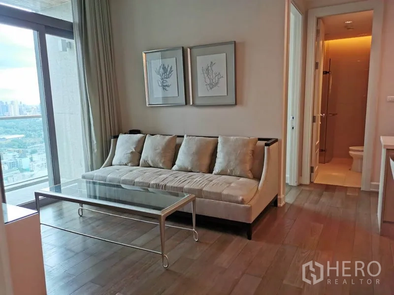 Condominium for rent in Pathum Wan, Bangkok - Bright living room with plush sofa, glass coffee table and a balcony city view.