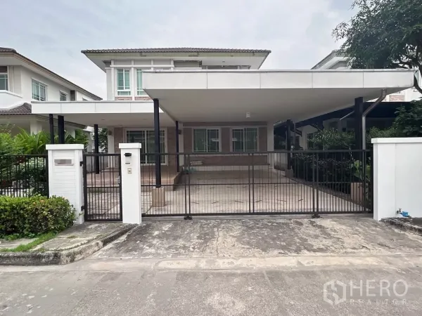 Detached House for sale in Bang Kapi, Bangkok - Front view of a two-storey detached house with wide covered carport and metal gate in a gated community.