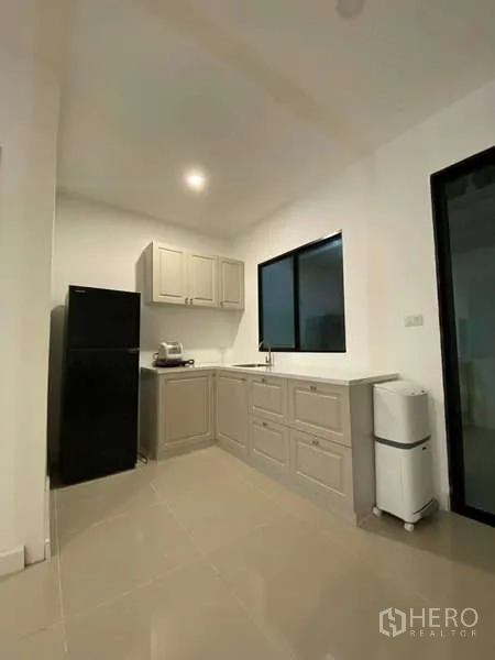 Townhouse for rent in Bang Kapi, Bangkok - Compact corner kitchen with grey cabinets, refrigerator, sink and window.