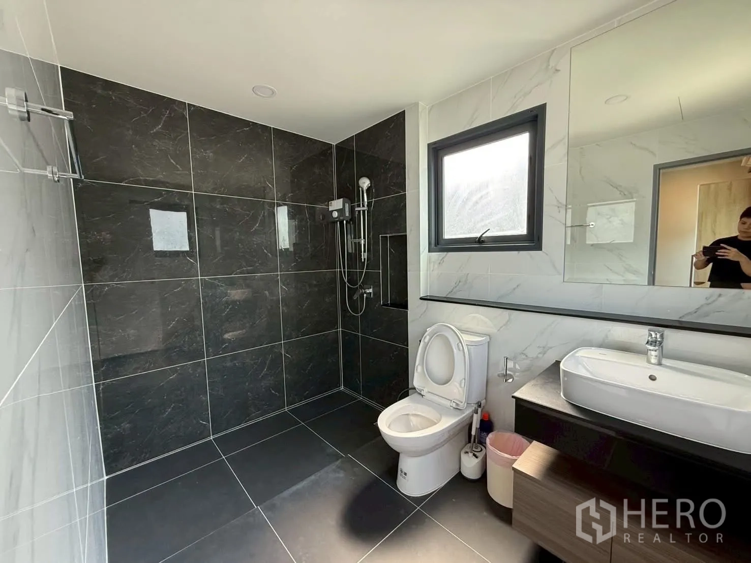 Townhouse for rent - Bathroom with dark tiled walk‑in shower, toilet and window; person in reflection ignored.